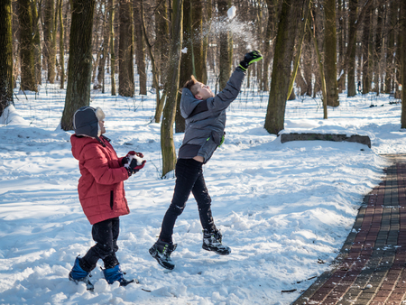 Two little boys throw snow up and have fun in winter parkの写真素材