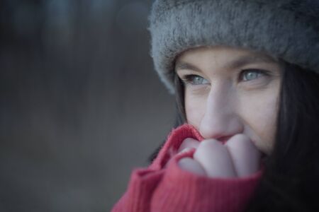 Extreme close-up of young beautiful brunette woman warming hands with breathe. Portrait of happy girl with grey eyes outdoors. Beauty, lifestyle, leisure.の写真素材