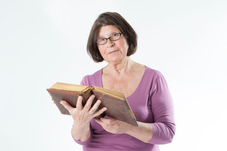 Elderly woman with an old book in her hands.Studio photography on a light gray background.の写真素材