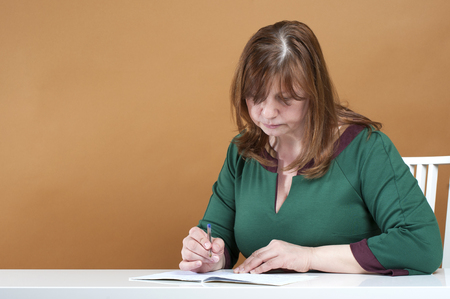 Middle-aged woman checks the notebook.
Studio photography on a light brown background.の写真素材