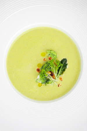 Cream of broccoli soup, served with pine nuts close-up in a white plate.の写真素材