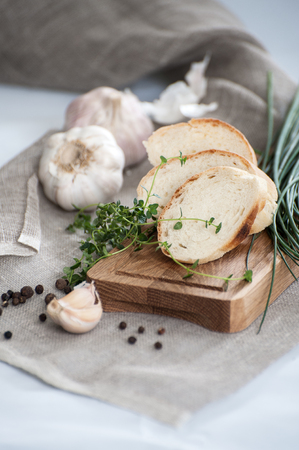 Three pieces of French baguette on a wooden board and fresh herbs.の写真素材