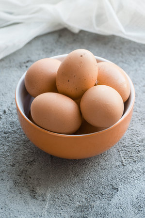 Brown chicken eggs in a bowl on a gray stone table.