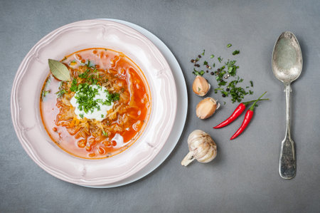 Cabbage soup with tomatoes in a plate and an old vintage spoon on a gray stone table.