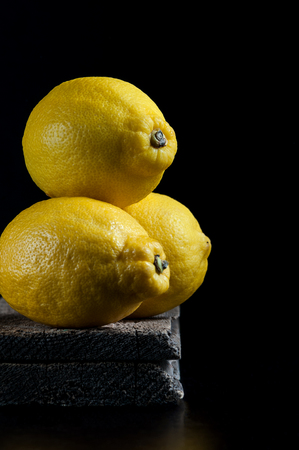 Three ripe lemons on old wooden boards on a black background. Shooting in the style of "dark mood".の写真素材