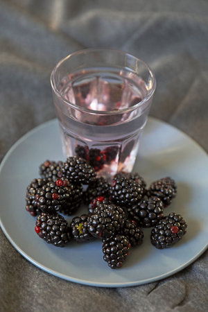Juicy blackberries on a blue plate with a glass of waterの写真素材