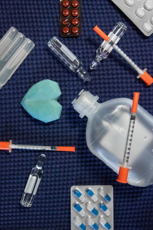 Flat lay composition of various medical items and medications arranged neatly on a blue background. Includes pills, capsules, syringes, ampoules and diagnostic tools. Concept of healthcare, treatment, pharmacy, and modern medicineの写真素材