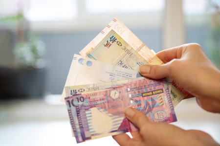 Woman holding a fan of Hong Kong dollar banknotes. Financial transaction and money currency concept. Exchange rate and foreign cash for travel.の写真素材