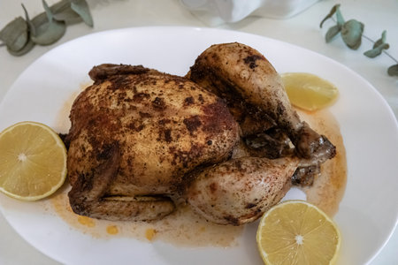 Whole roasted chicken served with fresh lemon slices on a white dish. Delicious home cooking and...