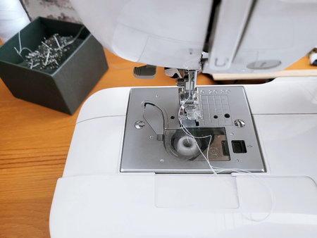 Close up of a modern sewing machine with white thread and bobbin. Needle plate and presser foot...