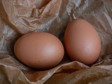 Two brown chicken eggs on a crumpled brown paper background showcasing natural food ingredient for...