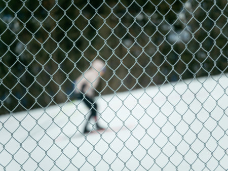 Chain link fence in foreground with blurred person ice skating in background. Winter recreation...