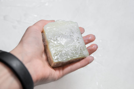 Hand of a woman holding a bar of natural soap with bubbles, concept of hygiene and skin care for...