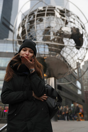 Young caucasian woman blowing air kiss in front of large metallic globe sculpture. Travel and global...