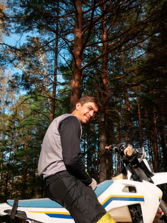Motorcyclist sitting on dirt bike in forest. Smiling man enjoying off road motorcycle ride in nature. Extreme sport and active lifestyle hobby in woodland on sunny autumn day.の写真素材
