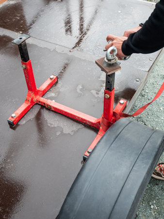 Man adjusting red metal stand on trailer floor. Mechanic securing equipment with ratchet strap....