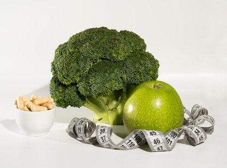 Green broccoli, apple, nuts and measuring tape on a white backgroundの写真素材
