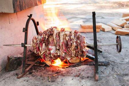 fresh lamb meat on an open fire on skewer for roasting-jack. daylight, wooden blocks are visible in the backgroundの写真素材