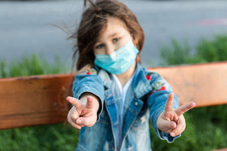 Caucasian girl sitting on a bench in the mask on the face with sad eyes and shows hands gesture vivaの写真素材