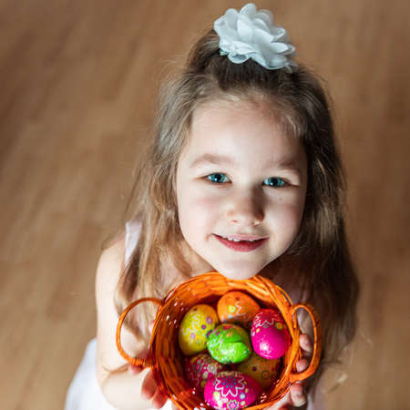 caucasian girl holding multicolored chocolate eggs in a basket and looking upwards into the cameraの写真素材