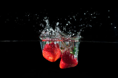 Strawberries splashing into water on a black backgroundの写真素材