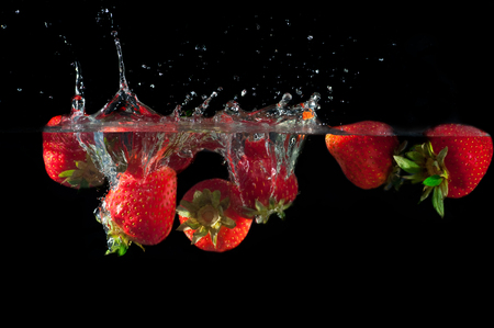 Strawberries splashing into water on a black backgroundの写真素材