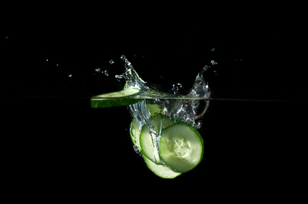 Sliced cucumber splashing water on black backgroundの写真素材