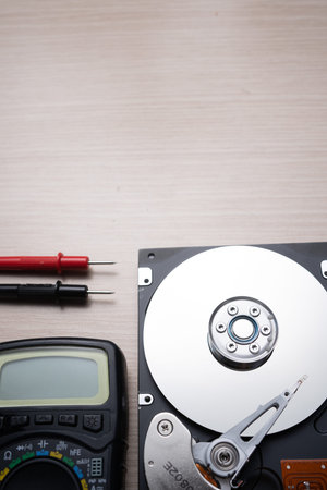 on the table lies an opened old hard drive and a multimeter for checking and repairing it