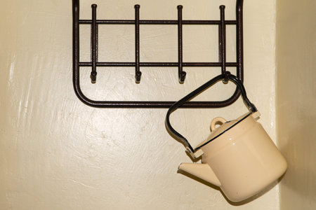 an old yellow metal kettle hangs on the wall on an empty clothes hanger