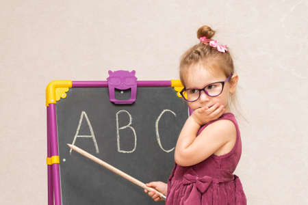 a girl in a dress and glasses near the blackboard shows students the letters in the alphabetの写真素材