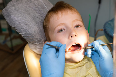 in the dental office, a 7-year-old child is examined with special tools. Dentist wearing medical...