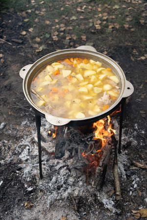 chicken chowder made of chicken wings and vegetables is cooked on a fire during outdoor recreation in a cauldron. In the soup, the vegetables are coarsely chopped and look very appetizing.の写真素材