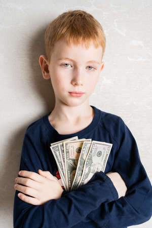 a red-haired boy leaning with his arms crossed on his chest holds the first earned money, dollars. The look of a confident personの写真素材