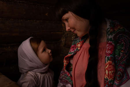 a woman and a baby in Russian folk costumes in a bast hut look at each other. Mom smiles at her daughter.の写真素材