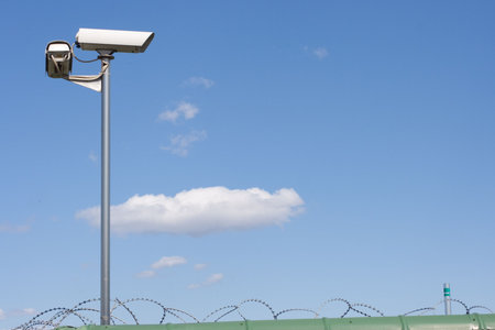 Surveillance camera on the wall with barbed wire on blue sky bacground