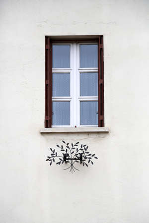 Beautiful wooden frame window in old building without people. Old building consisting of frame window view to garden with green leaves on trees. Frame window at old brick building on long street.の写真素材