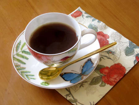 Beauty coffeecup standing on wooden table with dark tasty coffee. Brown old table consisting of liquid coffee in coffeecup, golden spoon, small plate. Porcelain coffeecup for coffee at antique table.の写真素材
