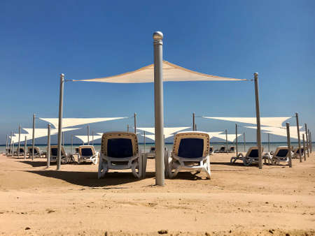 Stylish lounger in yellow sand to sun sunbed on beach in summer under open sky. Sunbed intended for cold shadow on convenient lounger. Fashion lounger with umbrella, plastic sunbed during hot weather.の写真素材