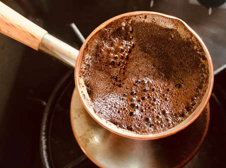 Barista preparing hot tasty drink from copper turk, boils water for coffee on small fire in cezve. Coffee turk made of organic copper, cezve to kitchen. Copper turk for real gourmet coffee at cezve.の写真素材