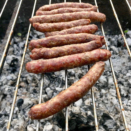 Barbecue with fiery Bavarian sausages on grill in garden outdoors. Grill consisting of collection sausages, accessory barbecue from meat cow. Roast sausage to light grill is tasty natural barbecue.の写真素材