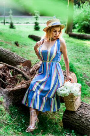 Beautiful girl wearing blue dress and hat collect flowers in basket in the wood.の写真素材