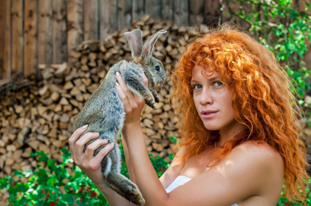 Beautiful girl with red hair on nature with a rabbit in her handsの写真素材
