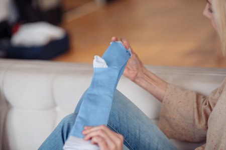 A woman sitting on the floor and putting on white cozy cotton socks on her feet, warming legs and body in autumn and winter. High quality photoの写真素材