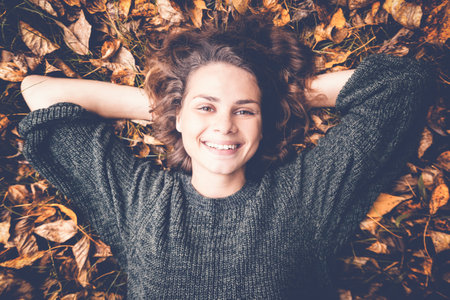 Young beautiful woman lies on autumn foliage in the park
