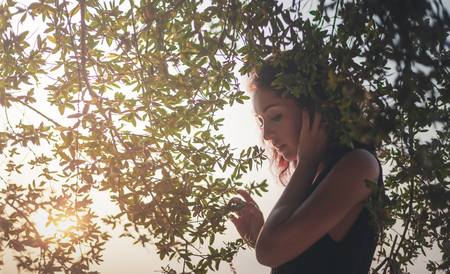 Portrait of a beautiful young woman with dark hair in a frame of branches and green leaves, summer and spring sensual portrait, natural beautyの写真素材