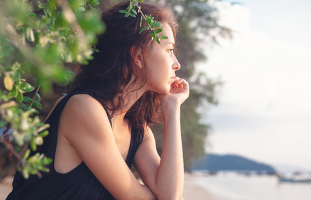 Portrait of a beautiful young woman with dark hair in a frame of branches and green leaves, on the coast, sensitive portrait of a natural beautyの写真素材