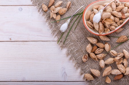 Almonds in their skins and peele in brown bowl on wooden background.の写真素材