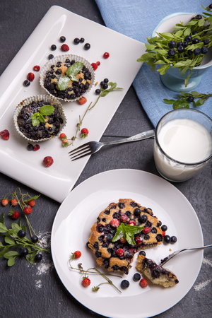 Berry muffin with blueberries and strawberries on a white plate and a wooden table served with milk and and fresh berriesの写真素材