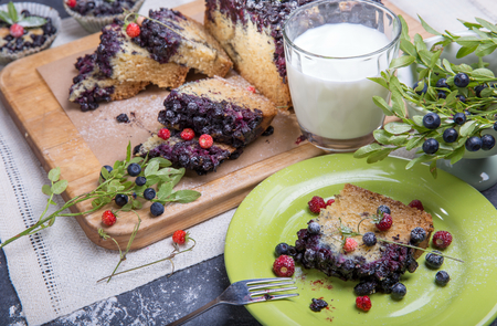 Berry cake and muffins with blueberries and strawberries on a green plate and a wooden desk served with milk and and fresh berriesの写真素材