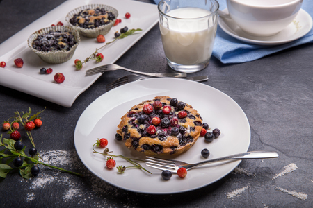Berry muffin with blueberries and strawberries on a white plate and a wooden table served with milk and and fresh berriesの写真素材